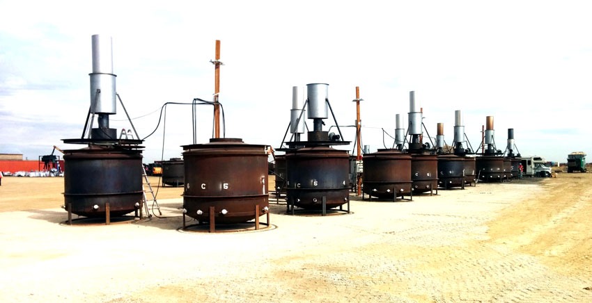 A row of pyrolysis kilns with emissions stacks on an open work site
